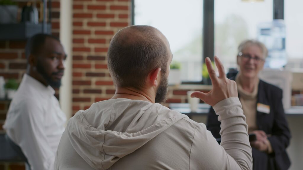Close up of man complaining about mental health problems at aa support group meeting. Person with addiction talking about depression with people in circle at rehab therapy session.