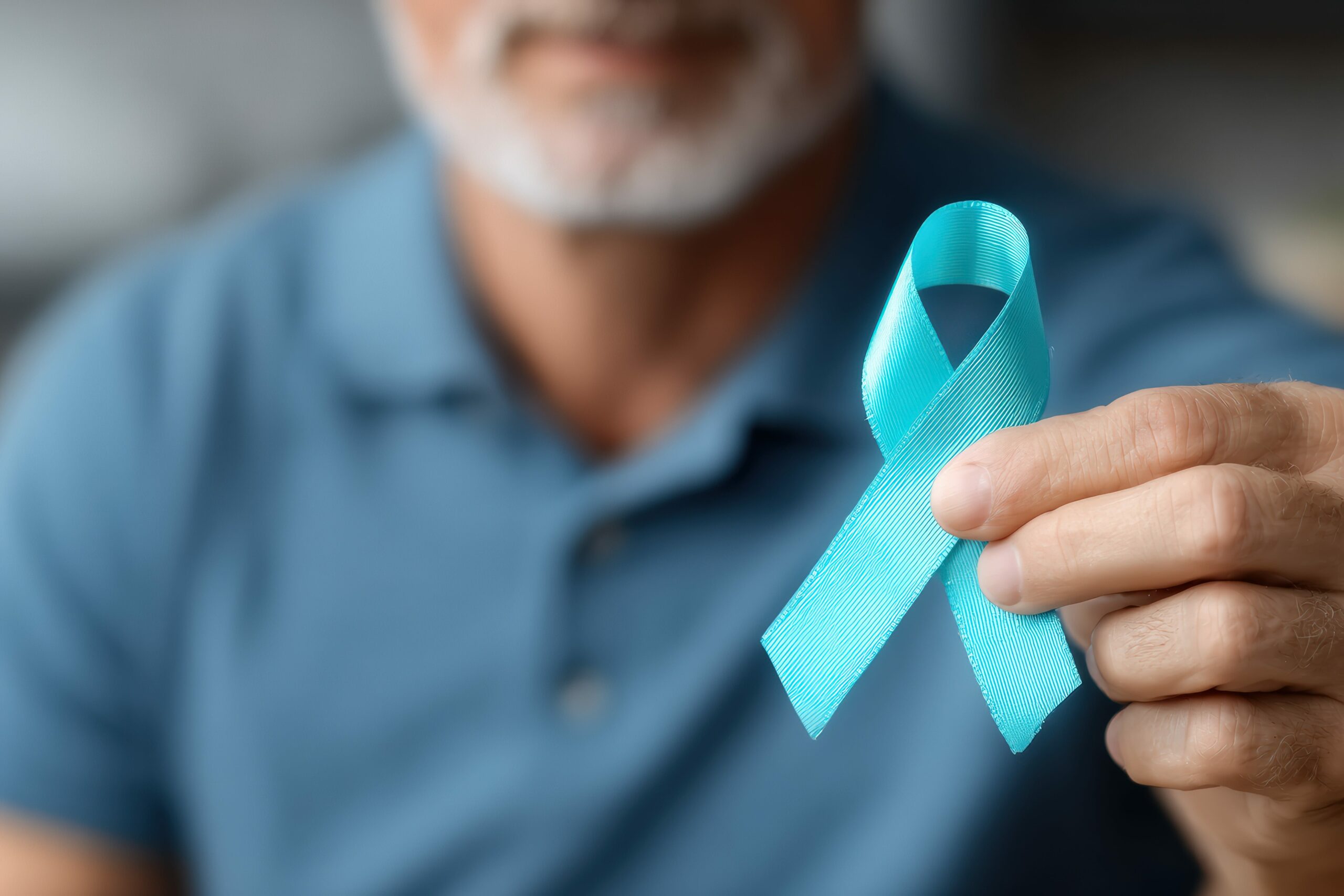 Mature man holding a light blue ribbon, symbolizing support for various social causes such as prostate cancer, addiction recovery, and awareness campaigns